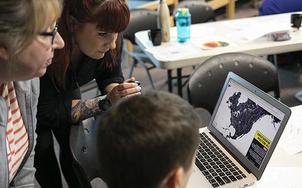 三位老师正看着笔记本电脑的屏幕，屏幕上显示着一幅带有移民模式的北美地图.